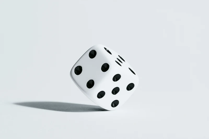 Black-and-white photograph of a die balanced on one edge above its shadow